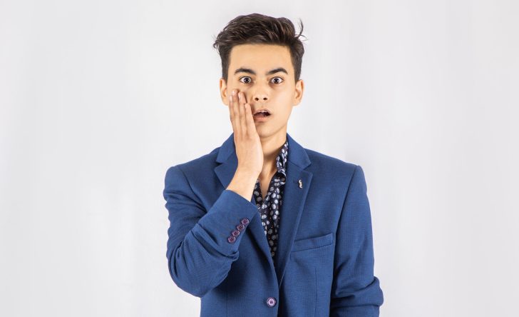 Photo of shocked man in blue blazer standing in front of white background